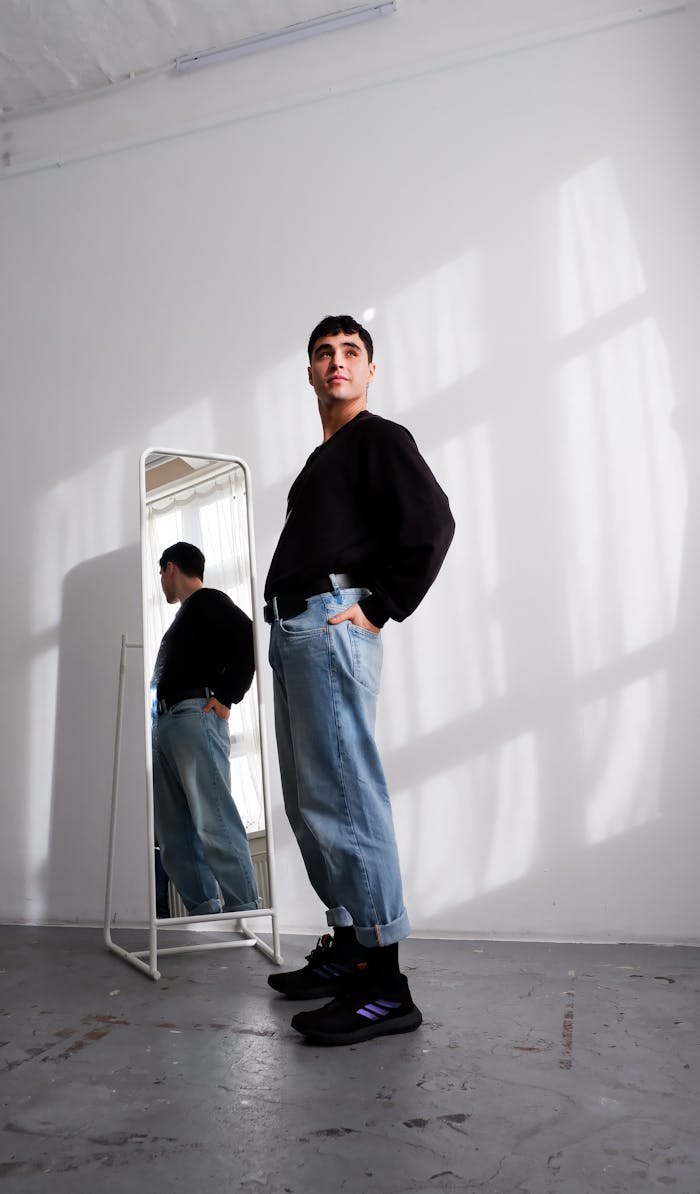 Fashionable man in jeans and sweater posing in bright indoor setting, Berlin.